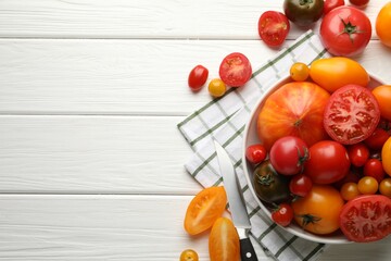 Different ripe tomatoes and knife on white wooden table, flat lay. Space for text