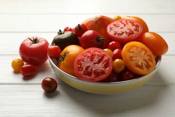 Many different ripe tomatoes on white wooden table, closeup