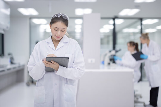 Femail scientist wearing a lab coat holding a tablet and smiling in a modern laboratory