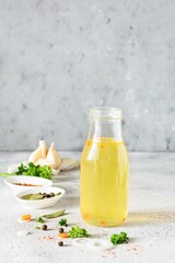 Homemade chicken, bone broth (bouillon) with vegetables, spices and herbs in a glass bottle on a light background. Natural collagen of animal origin. Liquid broth from meat, fish, vegetables.