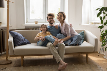 Smiling family of three cuddle on couch in living room