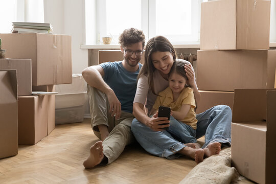 Happy couple with daughter using phone on floor among boxes