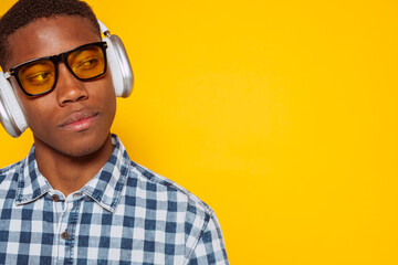 Obraz premium Stylish black latin american man wearing headphones and yellow glasses enjoying music on yellow background.