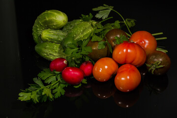 A still life of fresh vegetables on a dark, reflective surface. The black background and glare from...