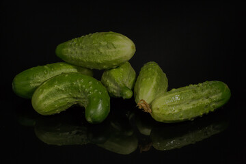 fresh cucumbers of different shapes and sizes lying on a dark, reflective surface. Some cucumbers have characteristic pimples and natural curves.
