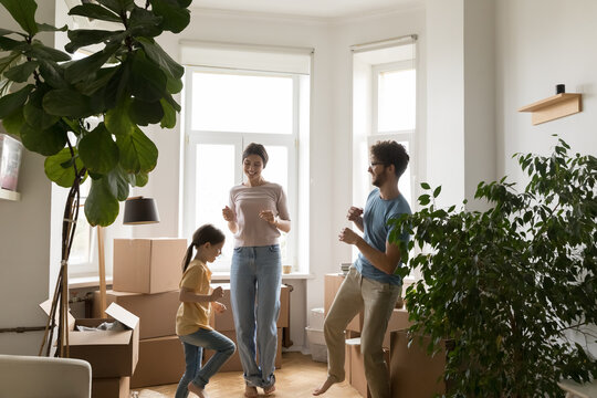 Excited couple with little daughter dancing celebrating buying new flat