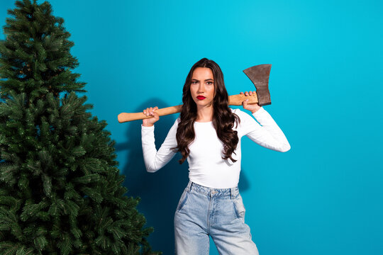 Cheerful stylish woman holding an axe next to a tree on a blue background, embodying an adventurous and trendy persona