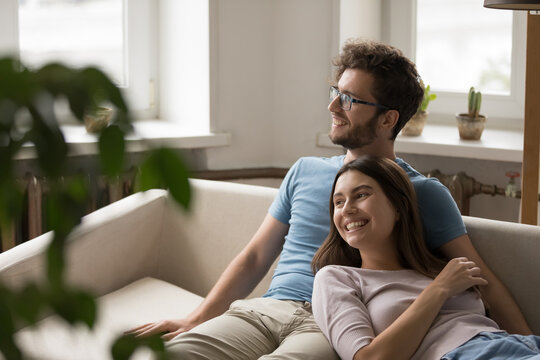 Dreamy wife lean back to smiling husband relaxing on sofa - Powered by Adobe