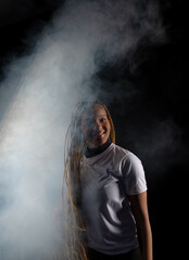 Obraz premium Portrait of a beautiful young woman with braided hair wearing a white outfit and posing for a studio photo. Isolated against a smoky background.