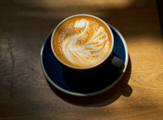 Cappuccino cup with one beautiful swan shape on the coffea foam on a wood table with a morning sunbeam.