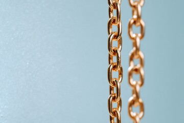 Fototapeta premium A vertical gold chain hangs elegantly against a soft gray-blue background, highlighting its intricate links and reflective surface