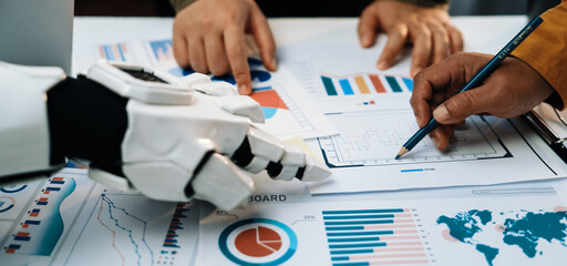 A human and a robot collaborate in a business meeting, analyzing various charts and graphs. This...