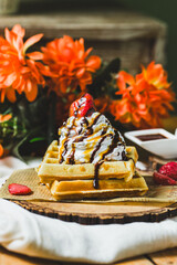 A golden-brown waffle topped with whipped cream, drizzled with chocolate sauce, and garnished with a cherry.