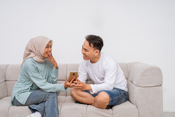 A joyful young couple shares a light moment on the couch while using a smartphone