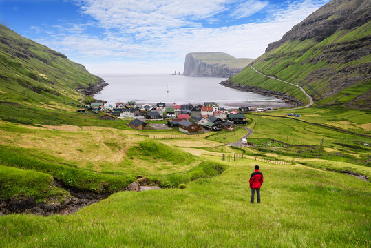 Tourist In Red Jacket Looking At Tjornuvik Village And Ocean, Faroe Islands