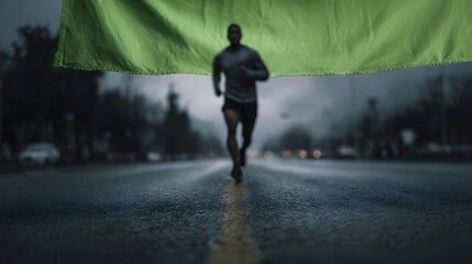 A determined man jogs along a wet city street beneath a green banner creating a powerful image of resilience and focus during his athletic endeavor