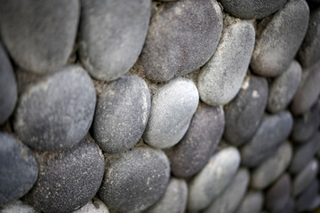 A close-up of a wall of natural gray and black river stones, arranged in a tight pattern to create a textured and organic background