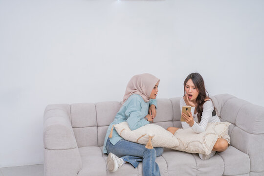Friends joyfully laughing and sharing a moment on the couch, each using their smartphone - Powered by Adobe