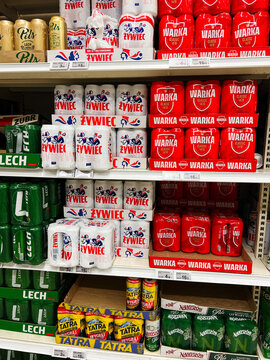 Variety of stacked polish beer packs displayed on store shelf showcasing colorful packaging