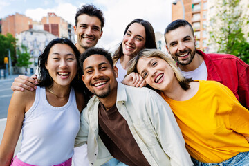 Diverse group of young people laughing at camera standing at city street. Portrait of happy multiracial students outdoors. Youth community concept.