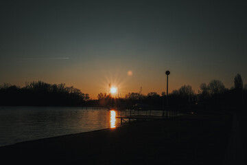 Fototapeta premium Winter warm sunset over Palic Lake in Serbia with calm water and silhouettes of trees and boats