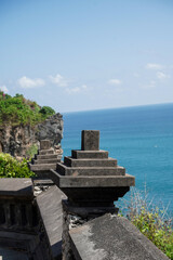 Fototapeta premium A close-up of a decorative Balinese stone monument on a balustrade, with the blue ocean and a lush green cliff in the background