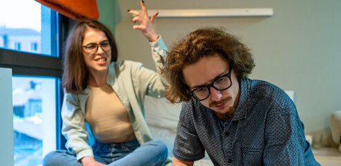 Young couple arguing at home. Angry woman gesturing emotionally, frustrated man looking down, feeling sad. Relationship conflict, emotional stress, communication problem, breakup tension.
