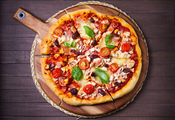 Delicious pizza served on wooden pizza board on brown background. View from above, top studio shot