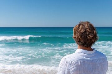 Fototapeta premium Man wearing white linen shirt gazes at waves on a sunny beach during afternoon