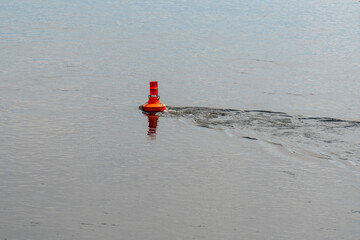 Bright orange buoy floating on the river. Navigation or safety marker used in water transport or recreational areas. Water safety, navigation