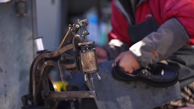 Worker operating vintage riveting machine to repair leather shoes in a workshop