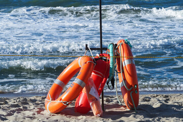 Fototapeta premium Water rescue equipment lies on the sand against the backdrop of sea waves. Lifebuoy, rescue float, line.