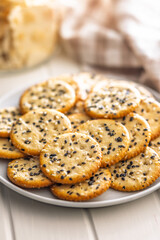 Crispy round salted crackers with sesame seeds on plate on white table.