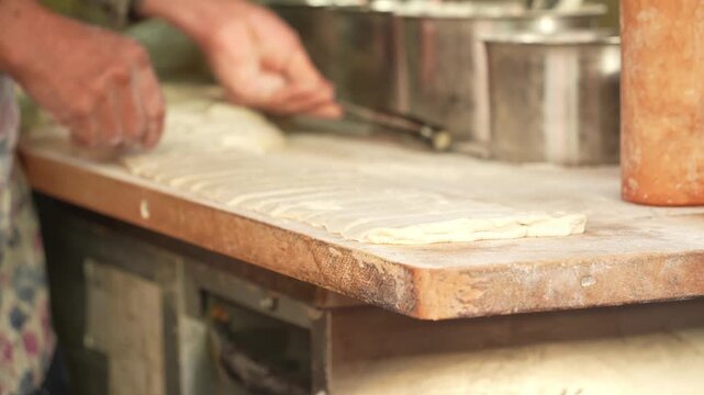 Chef manually rolling dough on a wooden counter to prepare traditional noodles or dumpling wrappers