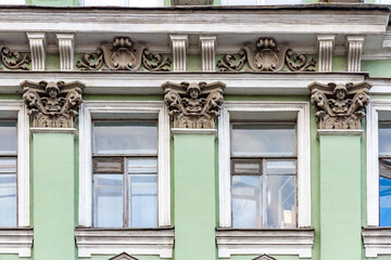 Decorative stucco facade with ornate window frames and sculpted capitals featuring human heads and floral motifs. Classical architecture detail in pastel green. Saint Petersburg, Russia