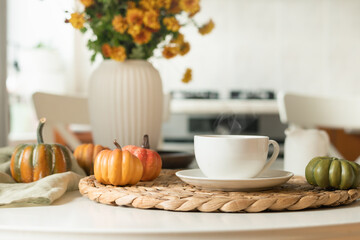 Warming autumn tea in white cup, orange flowers in vase at modern kitchen. Cozy home interior with coffee break. Close up.