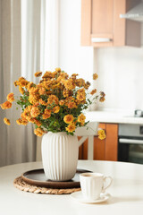 Autumn cozy home interior with coffee in white cup. Beautiful bouquet of orange flowers in vase at modern kitchen. Season cozy decoration at home. Close up.