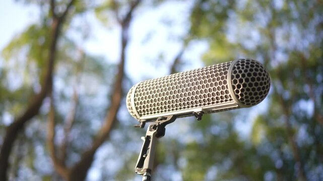 Professional microphone with metal grille and windscreen in outdoor forest background with bokeh effect