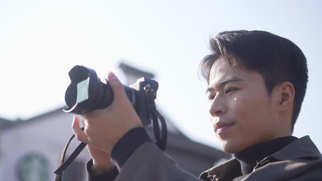 Young man holding camera and focusing intently while shooting street scenery outdoors