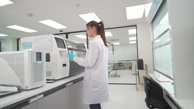 Female scientist looking trough the Integrated Staining and Coverslipping Workstation. That provides high-quality staining and superb glass coverslipping, with reliable equipment & optimized workflow