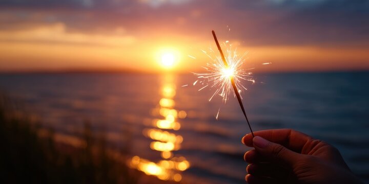 Hand holding sparkler at sunset on beach