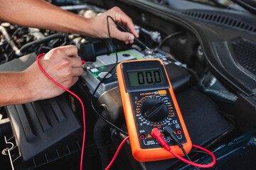 Testing car battery voltage with a multimeter during routine vehicle maintenance at a garage