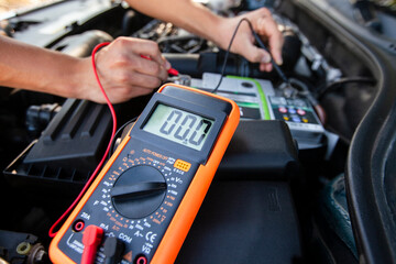 Car battery testing using a multimeter at a roadside in bright daylight