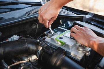 Man works on car battery maintenance in bright sunlight at a roadside location