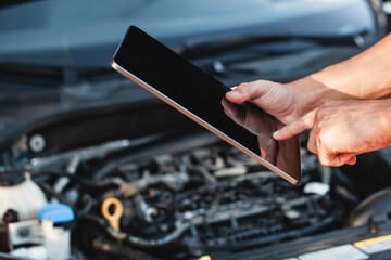 Technician using tablet to troubleshoot car engine issues during daytime in a garage