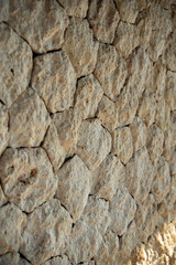 Angled close-up of a textured natural stone wall. The rough, beige rocks create a rustic and solid background with detailed shadows and depth