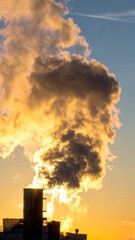 Dramatic Smoke Plume Rising from Industrial Chimney Against Golden Sunlight and Blue Sky at Dusk