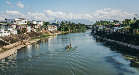 Fototapeta premium Small wooden banca boat navigating residential river canal under blue sky In Santa Cruz, Laguna Philippines
