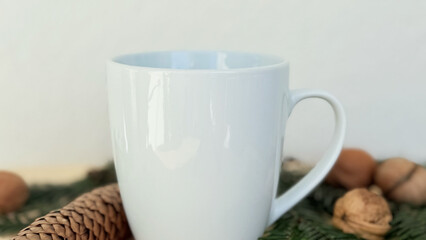 Close Up White Mug With Pine Cones and Walnuts on Evergreen Branches — Cozy Winter Decoration, Minimal Mockup with Copy Space for Banner, Branding and Template Design