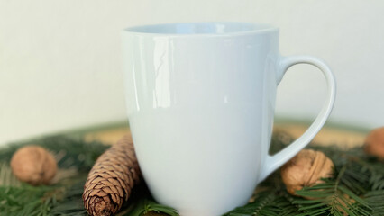 Close Up White Mug With Pine Cones and Walnuts on Evergreen Branches — Cozy Winter Decoration, Minimal Mockup with Copy Space for Banner, Branding and Template Design